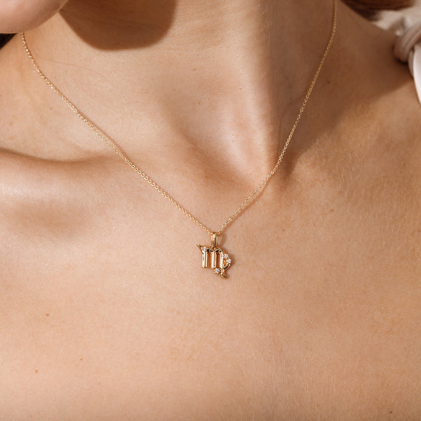 Close-up of a person wearing a delicate gold chain pendant necklace with a Virgo zodiac symbol charm pendant.