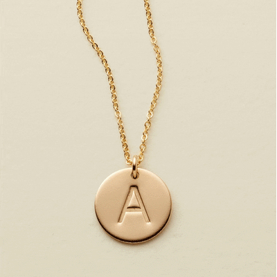 A gif of a delicate gold pendant chain with flat round disc pendants, each engraved with a single initial. The gif starts with a single disc, then continues adding one after another up to three discs.