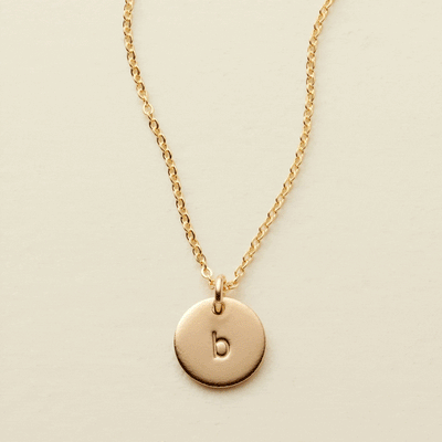 A gif of a delicate gold pendant chain necklace starting with a singular flat round disc charm engraved with a lowercase initial 'b', then adding more engraved discs one by one up to five.