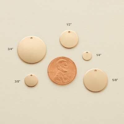 Five round gold flat discs in varying sizes laying flat around a penny for sizing reference. Each of the discs is labeled with a size, '3/8"', '3/4"', '1/2"', '1/4"', and '5/8"'.