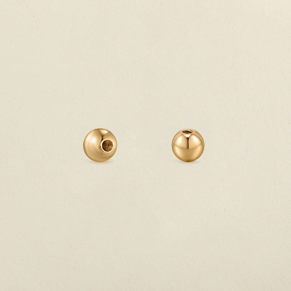 A pair of polished round gold screw-on earring backings, shown on a solid light beige surface.