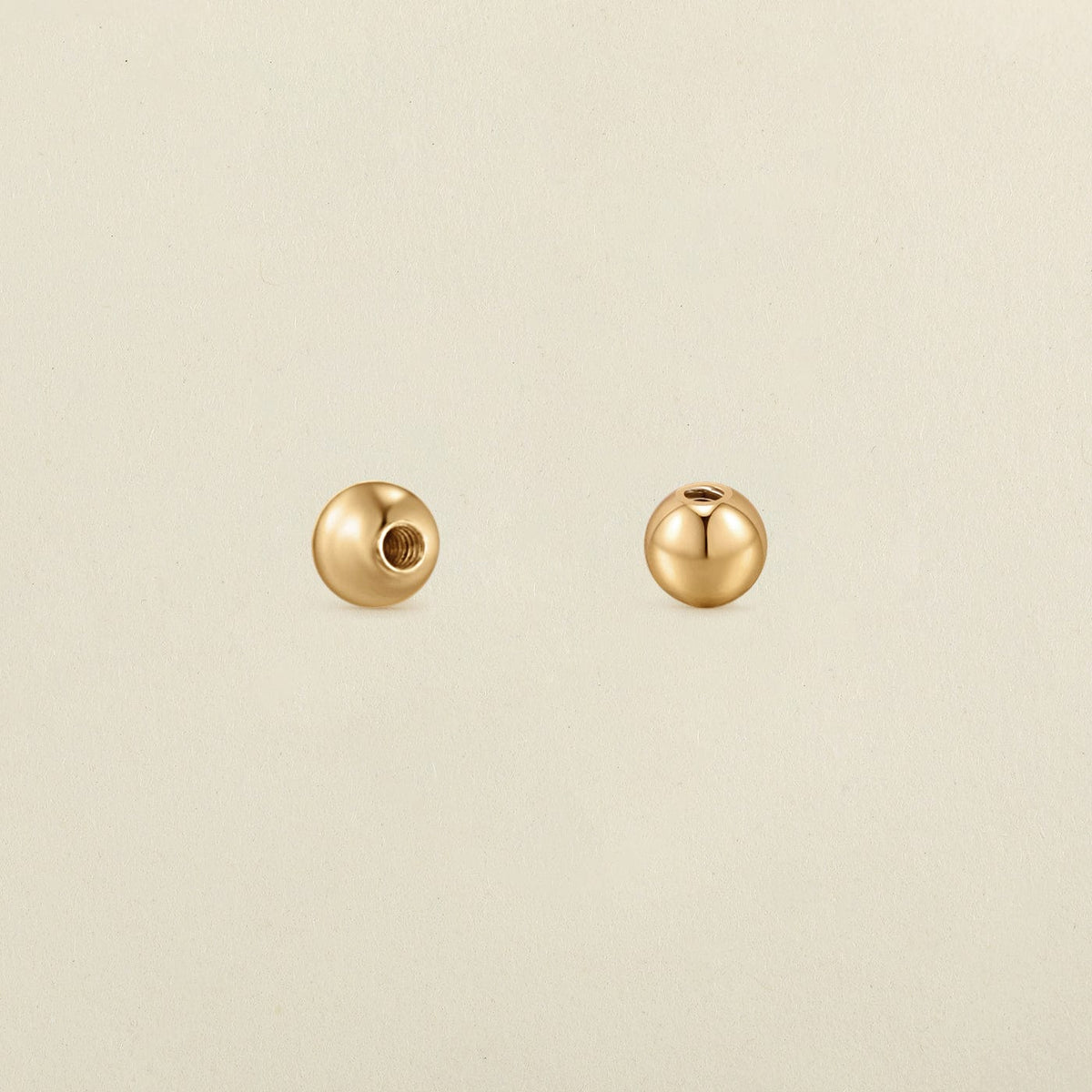 A pair of polished round gold screw-on earring backings, shown on a solid light beige surface.
