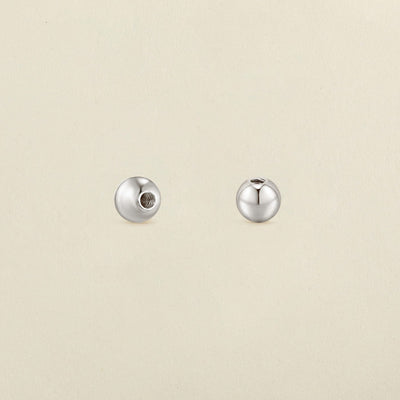 A pair of polished round silver screw-on earring backings, shown on a solid light beige surface.