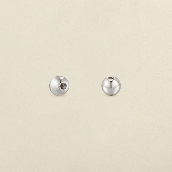 A pair of polished round silver screw-on earring backings, shown on a solid light beige surface.