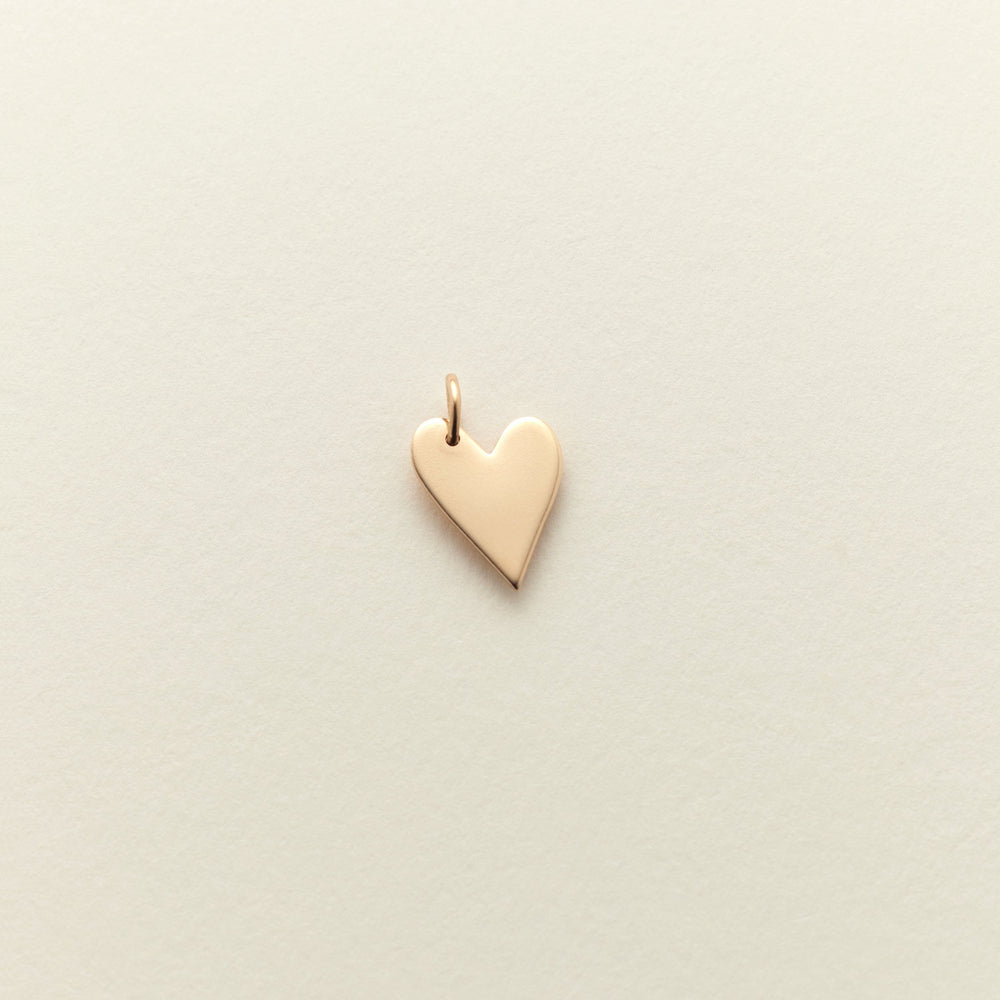 A small, polished gold heart charm with a delicate top loop, centered on a textured off-white background.