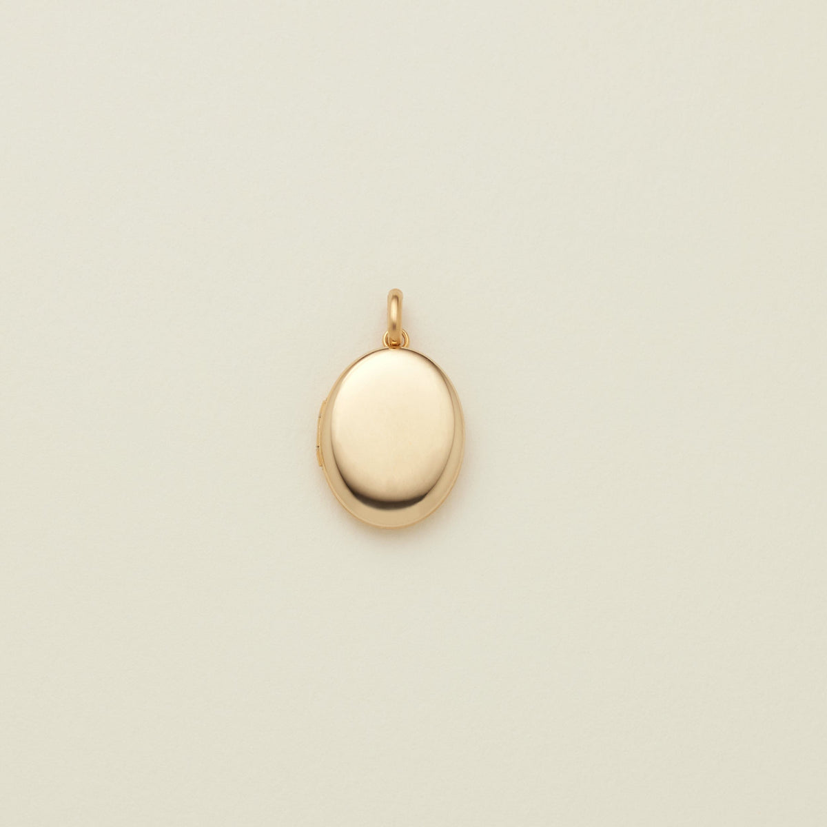 A small oval gold locket pendant with a polished finish and a top loop, centered on a light cream background.