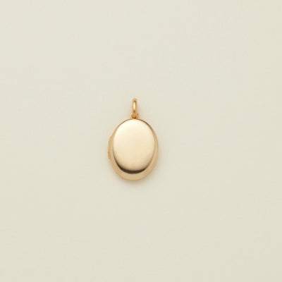 A small oval gold locket pendant with a polished finish and a top loop, centered on a light cream background.