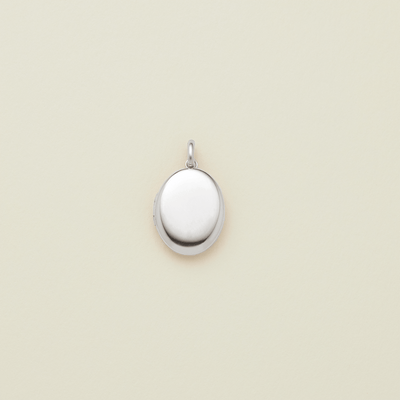 A small oval silver locket pendant with a polished finish and a top loop, centered on a light cream background.