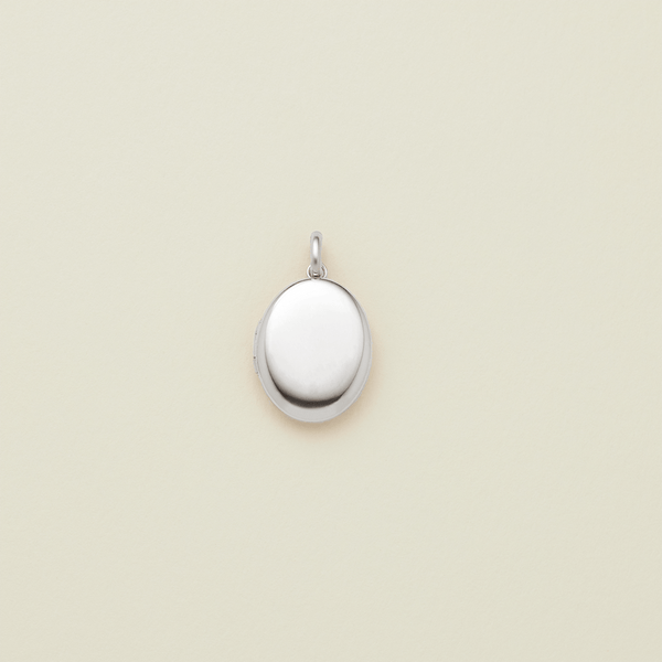A small oval silver locket pendant with a polished finish and a top loop, centered on a light cream background.