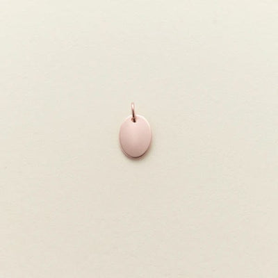 A small flat rose gold oval charm, shown against a solid light beige background.