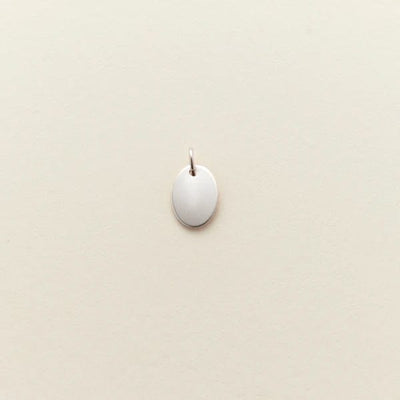 A small flat silver oval charm, shown against a solid light beige background.