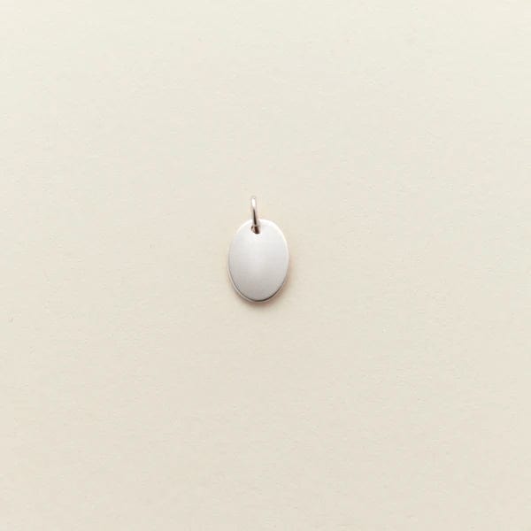 A small flat silver oval charm, shown against a solid light beige background.