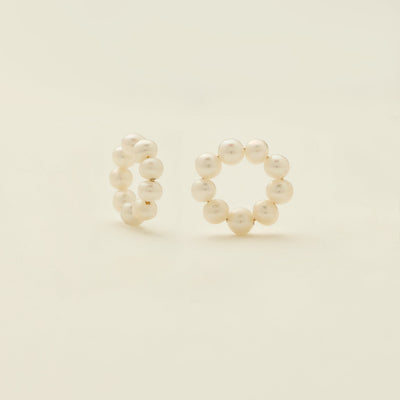 A pair of round ring hoop earring attachments, made-up of round cream colored pearls, shown on a solid light beige background.