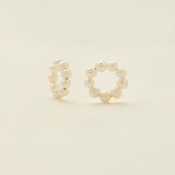 A pair of round ring hoop earring attachments, made-up of round cream colored pearls, shown on a solid light beige background.