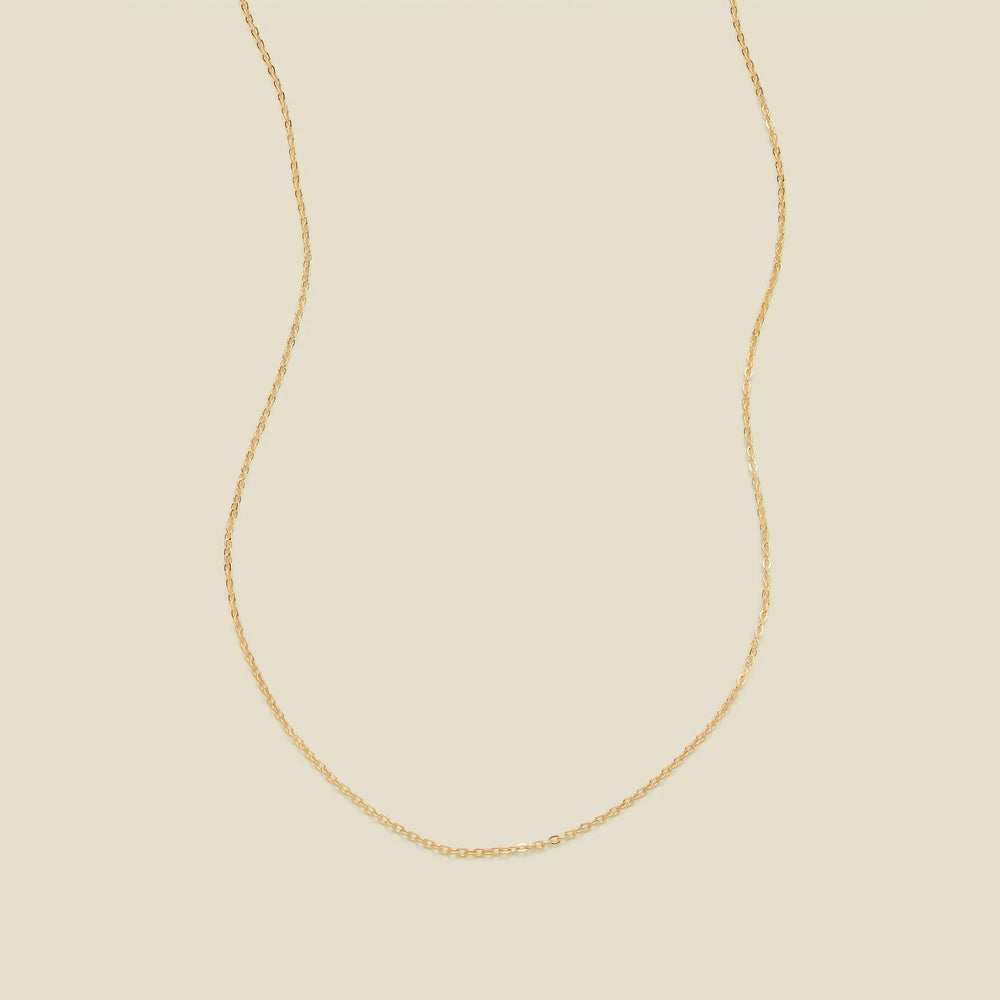 A delicate gold chain necklace arranged in a U-shape against a solid, warm beige background.