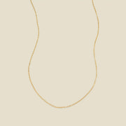 A delicate gold chain necklace arranged in a U-shape against a solid, warm beige background.