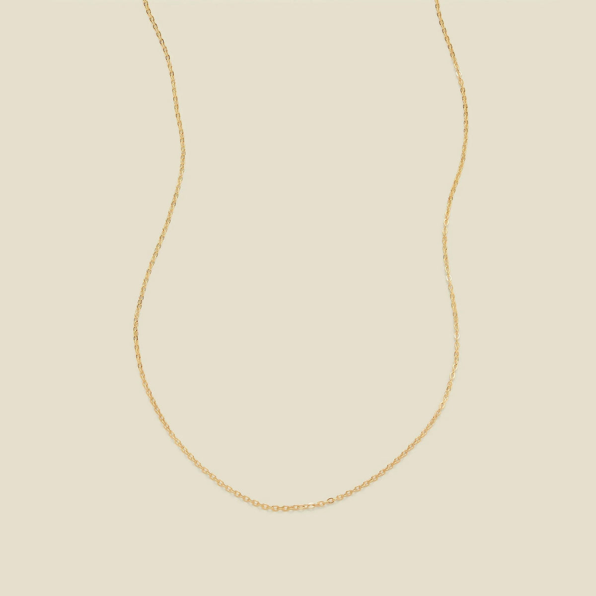 A delicate gold chain necklace arranged in a U-shape against a solid, warm beige background.