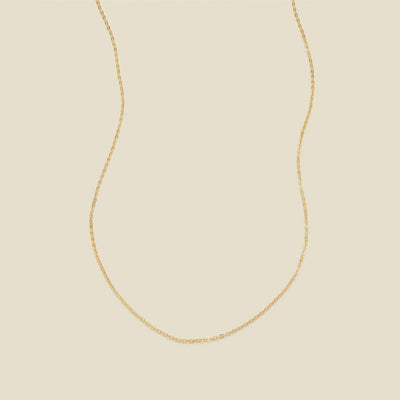 A delicate gold chain necklace arranged in a U-shape against a solid, warm beige background.