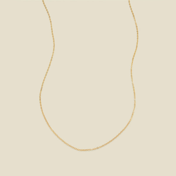 A delicate gold chain necklace arranged in a U-shape against a solid, warm beige background.