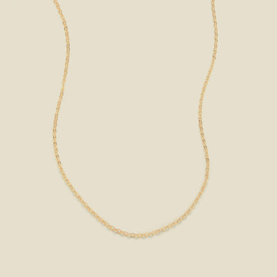 A delicate gold chain necklace arranged in a U-shape against a solid, warm beige background.