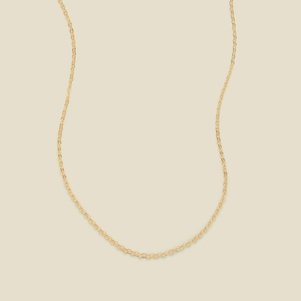 A delicate gold chain necklace arranged in a U-shape against a solid, warm beige background.