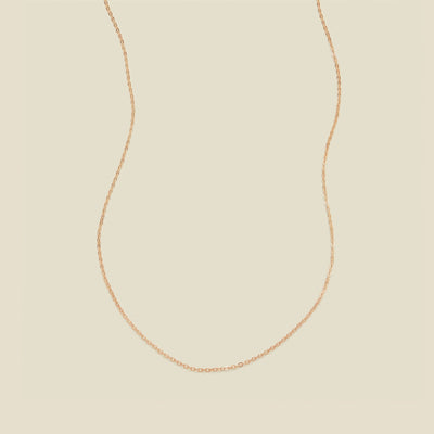 A delicate rose gold chain necklace arranged in a U-shape against a solid, warm beige background.