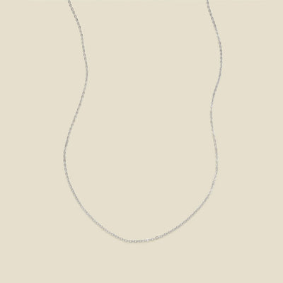 A delicate silver chain necklace in a U-shape, set against a solid light beige background.