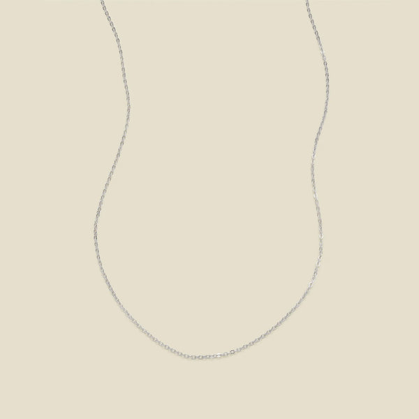 A delicate silver chain necklace in a U-shape, set against a solid light beige background.