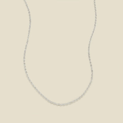 A delicate silver chain necklace arranged in a U-shape against a solid, warm beige background.