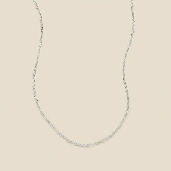 A delicate silver chain necklace arranged in a U-shape against a solid, warm beige background.