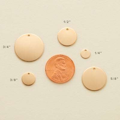 Five different sized round gold flat discs laying around a penny, showing the size comparison for each and labeled with the size of each disc. The sizes shown are 3/8", 3/4", 1/2", 1/4", and 5/8".