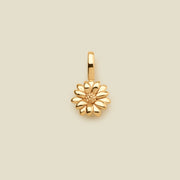 A small gold daisy flower charm, shown centered on a solid light beige background.