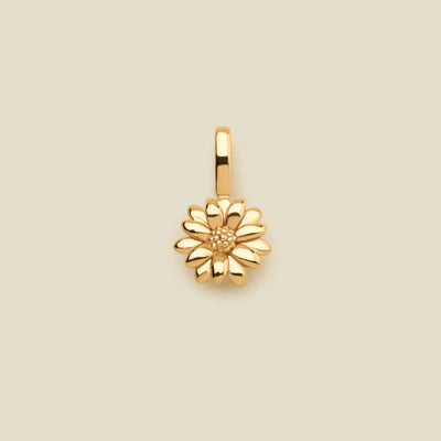 A small gold daisy flower charm, shown centered on a solid light beige background.