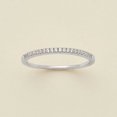 A silver ring featuring a single row of small round-cut clear gemstones, photographed on a clean, solid, warm off-white background.