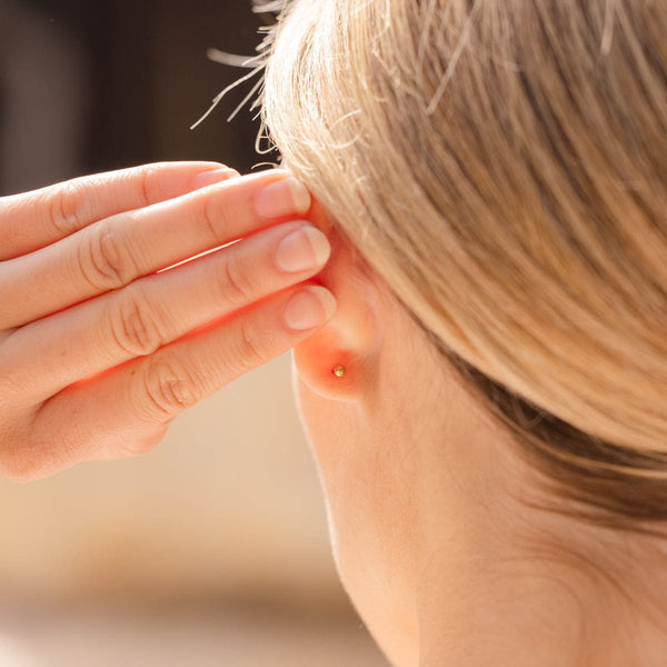 A close-up of the back of a person's ear wearing a round ball back stud.