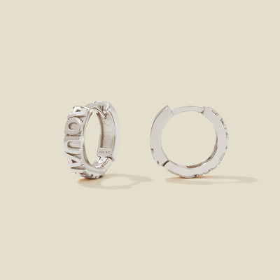 A pair of silver huggie hoop earrings on a light beige background. One earring is shown from the side, displaying a polished outer surface, while the other is shown from the front, showcasing the word 'AQUARIUS' in raised letters.