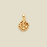 A small gold poppy flower charm, shown centered on a solid light beige background.