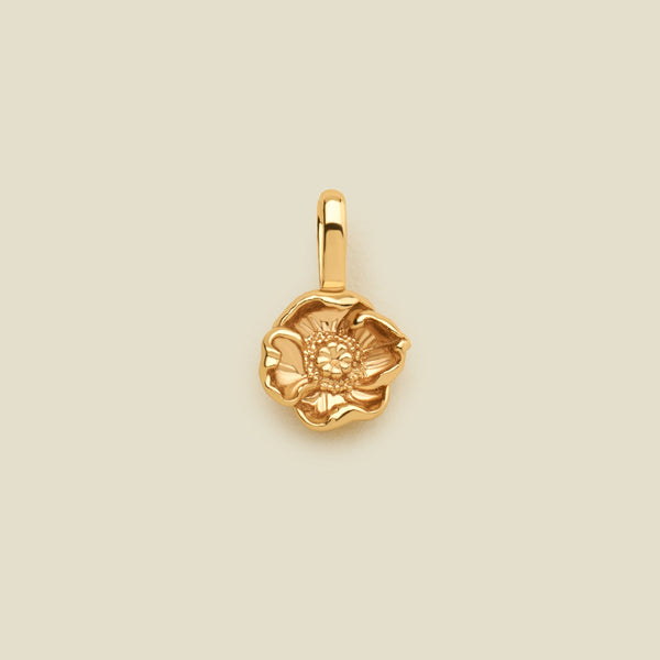 A small gold poppy flower charm, shown centered on a solid light beige background.