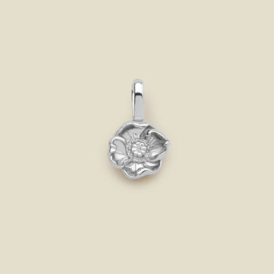A small silver poppy flower charm, shown centered on a solid light beige background.