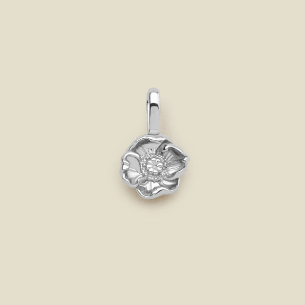 A small silver poppy flower charm, shown centered on a solid light beige background.