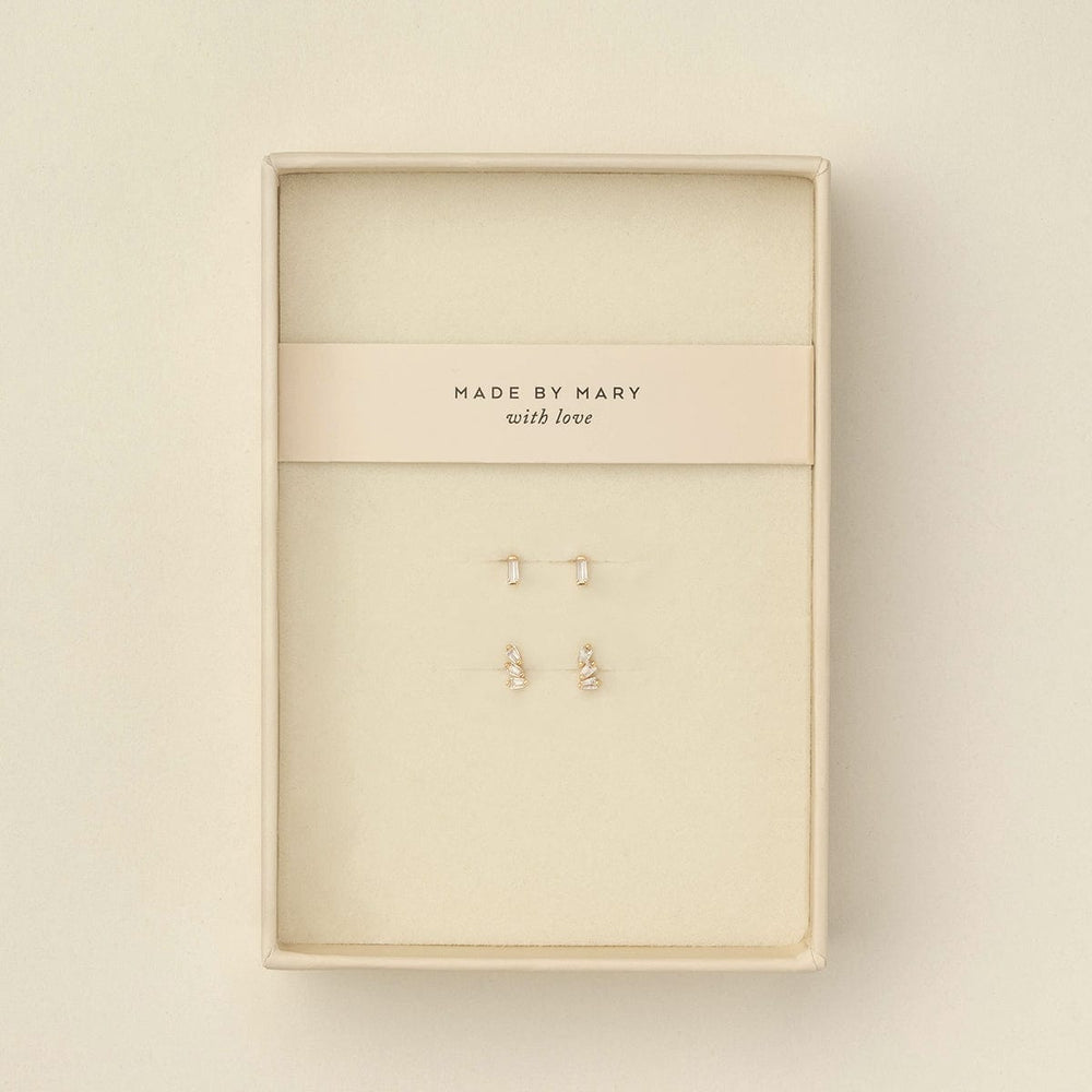 Two pairs of small gold stud earrings with baguette clear gemstone accents, displayed on a cream-colored jewelry card inside a cream-colored presentation box. The card is printed with the brand name 'MADE BY MARY with love'.