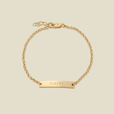 A gold chain bracelet with a horizontal bar engraved with the name 'CLAIRE', shown on a solid light beige background.