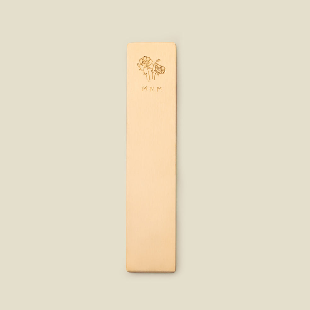 Gold bookmark with floral design and initials on a beige background