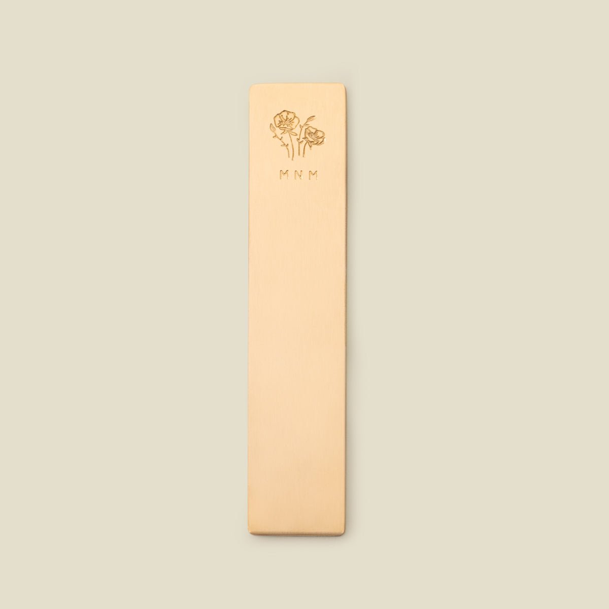 Gold bookmark with floral design and initials on a beige background