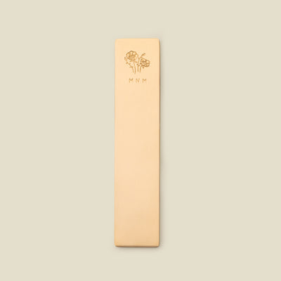 Gold bookmark with floral design and initials on a beige background