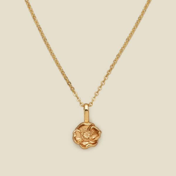 A gold pendant necklace with a small poppy pendant charm, shown on a solid light beige background.