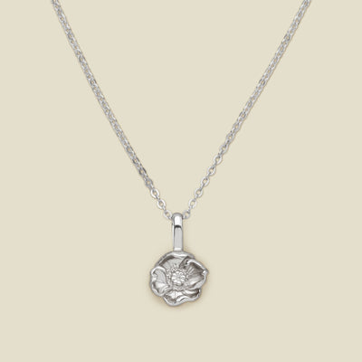 A silver pendant necklace with a small poppy flower charm, shown on a solid light beige background.