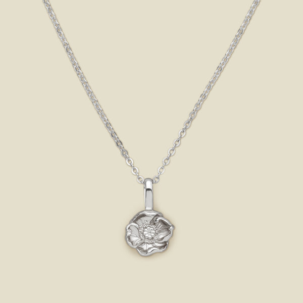 A silver pendant necklace with a small poppy flower charm, shown on a solid light beige background.