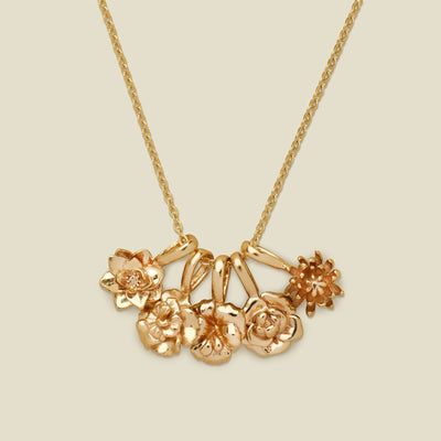 A gold pendant necklace with five small flower charms, shown on a solid light beige background.