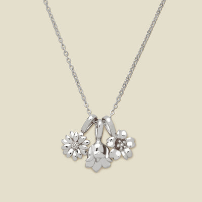 As silver pendant necklace with three small flower charms, shown on a solid light beige background.